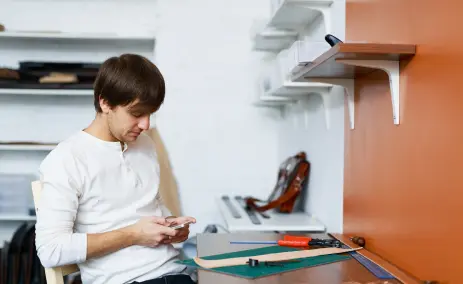 Man-sitting-at-a-desk-using-a-smartphone-with-tools-nearby
