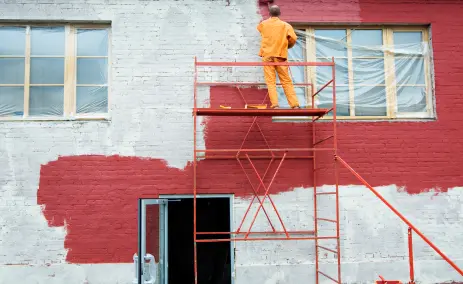 Worker-on-scaffolding-paints-a-wall-red-with-part-still-white