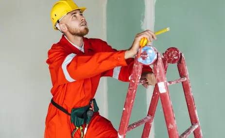 painter-in-red-overalls-on-a-ladder-measuring-a-wall